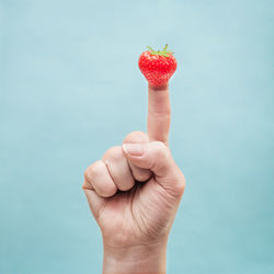 Close-up of finger with strawberry against blue background
