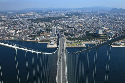 High angle view of suspension bridge over sea by cityscape