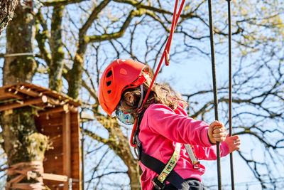 Little girl with protections practicing climbing between trees with ropes and nets