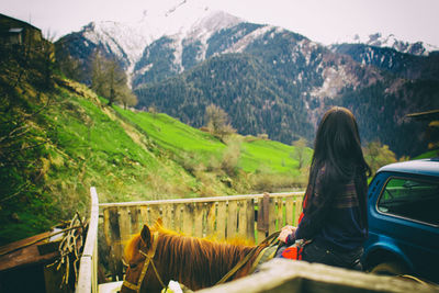 Woman riding horse by fence against mountains