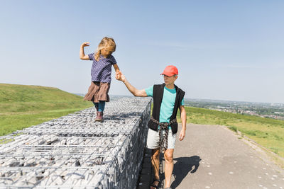 Grandfather walking with granddaughter on wall against sky