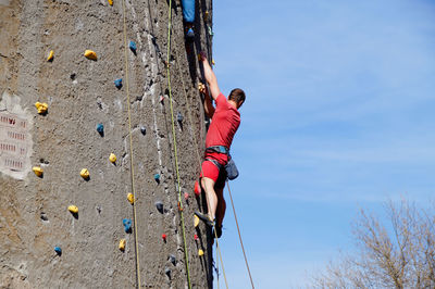 Low angle view of man rock climbing against sky