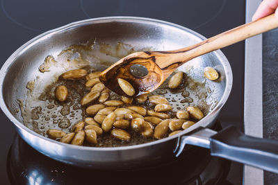 Cropped image of hand preparing caramelized almonds in cooking pan