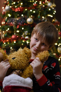 Boy playing with stuffed toy in front of christmas tree