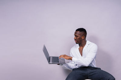 Young woman using laptop while sitting against white background