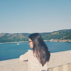 Rear view of young woman standing by retaining wall against clear sky