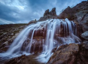 View of waterfall against cloudy sky