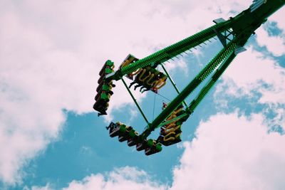 Low angle view of people in amusement park ride against cloudy sky