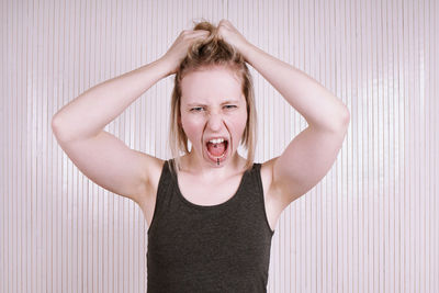 Portrait of young woman screaming against blinds