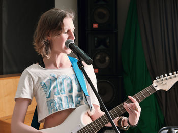 Young woman musician playing guitar in studio during rehearsal. rock musician smiling 