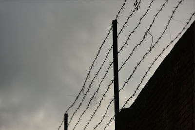 Low angle view of barbed wire fence against sky