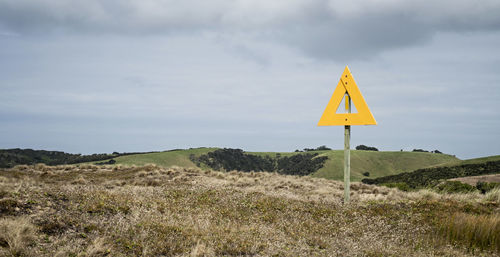 Directional sign on field against cloudy sky