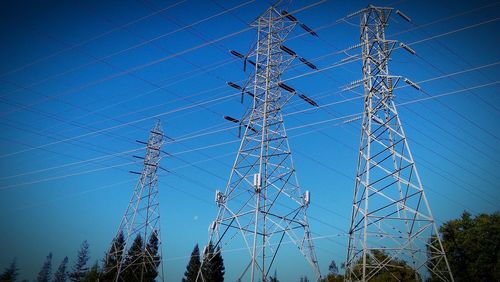 Low angle view of electricity pylon against blue sky