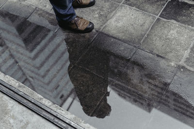 Low section of man standing by puddle on footpath