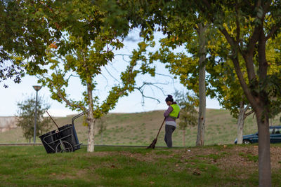 Woman with broom standing on field against trees