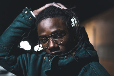 Close-up portrait of man wearing eyeglasses in illuminated city at night