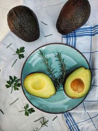 Fresh avocado with herbs and lemons lies on the table on blue plate on white background. flat lay