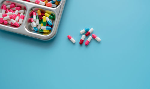 High-angle view of multi-colored antibiotic capsule pills on stainless steel tray and blue 