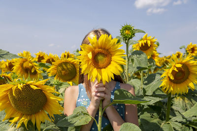 Girl holding sunflower in front of her face in the field. generation z.