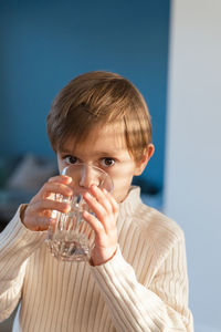 A child drinks water from a glass in the living room.