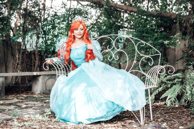 Full length of woman with red hair sitting on seat outdoors