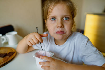 Cute girl eats yogur with appetite, has dirty mouth, has fun, grimaces