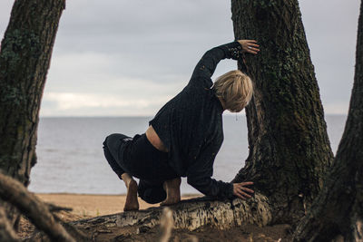 Reflection of man on tree trunk by sea against sky