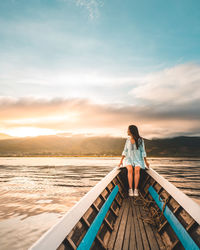 Woman looking at view while sitting on boat in lake against sky during sunset