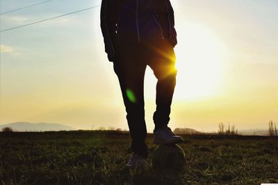 Low section of man standing on field against sky during sunset