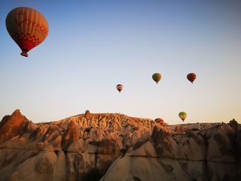 Hot air balloons flying over rocks against clear sky