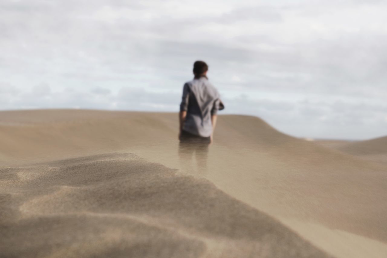 REAR VIEW OF MAN ON SAND DUNE
