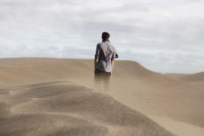 Rear view of man on sand at beach against sky