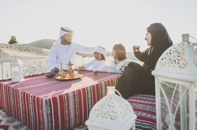 Happy family having tea on carpet at desert