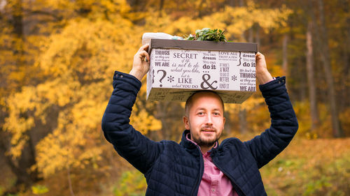 Portrait of man holding box against trees
