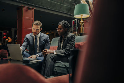 Young businessman discussing over laptop with female colleague sitting in hotel lounge