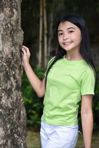 Portrait of a smiling young woman standing on tree trunk