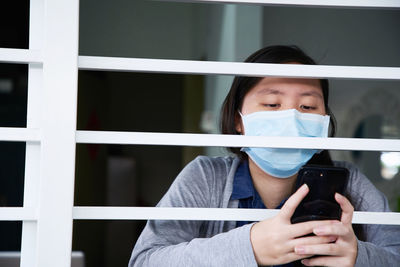 Portrait of young woman wearing face mask holding mobile phone