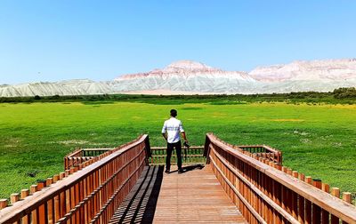 Rear view of man standing on railing against mountain