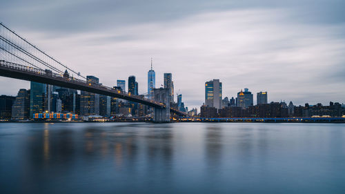 Bridge over river by buildings against sky in city