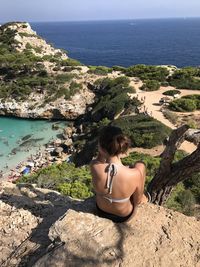 Rear view of woman sitting on rock by sea