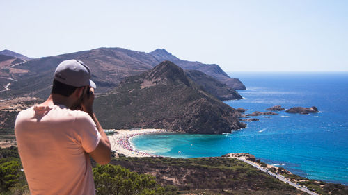 Rear view of man looking towards sea and mountains