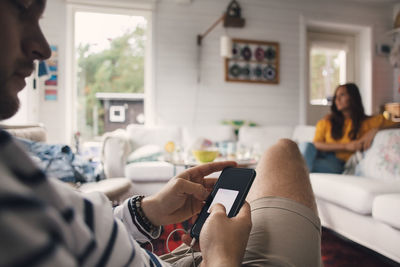 Man using mobile phone against woman sitting on sofa at home