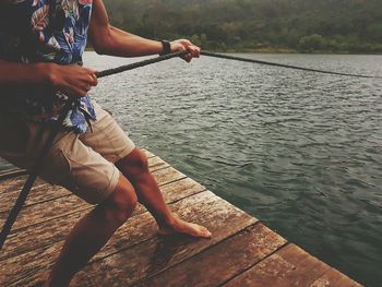 Low section of man pulling rope while standing on pier over lake