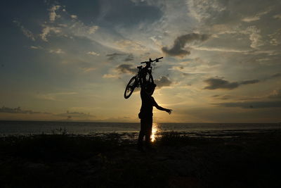 Silhouette man holding umbrella at beach against sky during sunset