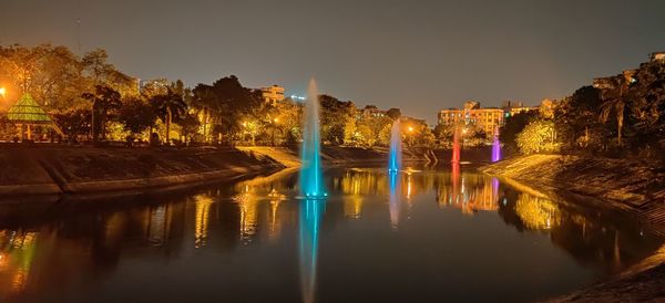 Illuminated buildings by river against sky at night