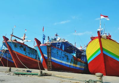 Fishing boats moored on beach against blue sky