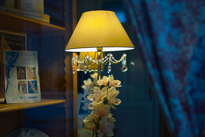 Close-up of illuminated lamp on table against wall at home