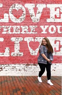 Full length portrait of woman standing against brick wall