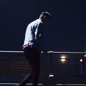 Man standing on railing against illuminated city at night