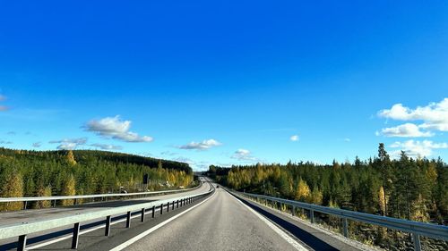 Road amidst trees against blue sky